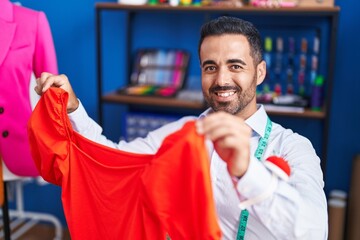 Sticker - Young hispanic man tailor smiling confident holding clothes at sewing studio