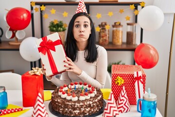 Sticker - Hispanic woman celebrating birthday with cake holding present puffing cheeks with funny face. mouth inflated with air, catching air.