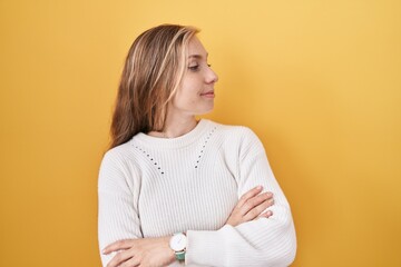 Wall Mural - Young caucasian woman wearing white sweater over yellow background looking to the side with arms crossed convinced and confident