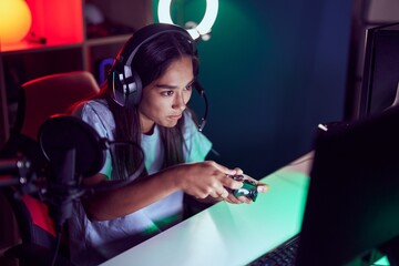 Wall Mural - Young beautiful hispanic woman streamer playing video game using joystick at gaming room