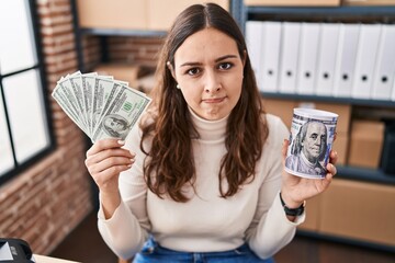 Sticker - Young hispanic woman working at small business ecommerce holding money and piggy bank skeptic and nervous, frowning upset because of problem. negative person.