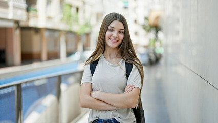 Sticker - Young beautiful girl student wearing backpack standing with arms crossed gesture smiling at school