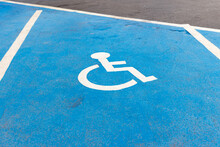 Parking for disabled or wheelchair. A sign indicates reserved parking for disabled people in a car park.  International handicapped symbol painted in bright blue on a shopping center parking space.