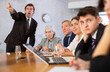 Dissatisfied adult manager reprimanding subordinates due to unfulfilled tasks sitting at table during work meeting