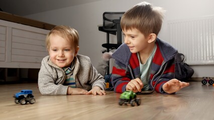 Two little brothers playing together with toy cars on floor. Children playing alone, development and education, games at home.