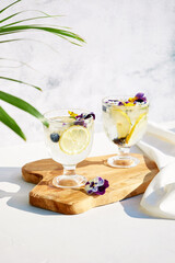 Wall Mural - Chilled cocktails with fresh citrus fruits garnished with edible flowers on a wooden serving board. Summer drinks with soda and fruit