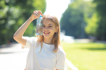  Portrait of beautiful teenager pretty girl, young thirsty woman is drinking pure fresh water from bottle at warm sunny summer day outdoors, holding a bottle near her eyes and smiling