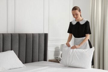 Poster - Young maid making bed in hotel room. Space for text