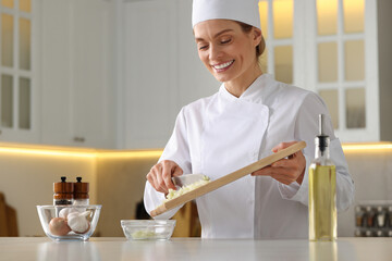 Wall Mural - Professional chef putting cut onion into bowl at white marble table indoors, low angle view