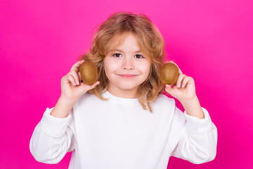 Wall Mural - Child hold kiwi in studio. Kiwi fruit. Studio portrait of cute kid boy with kiwi isolated on pink background.