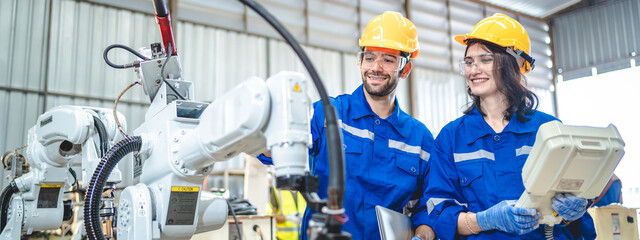 Wall Mural - Engineer people service robot working in automation factory. Worker team in safety suit work robotic arm software programming or replacing part in automated manufacturing industry technology