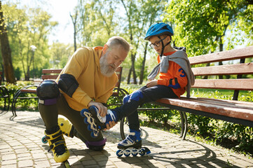 Father helping son to put on roller skates in urban park