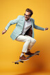 © AI_images - Young handsome funny man with glasses, brown hair and beard, wearing light grey suit and sneakers, jumping with the skateboard on color studio background.
