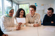 © Westend61 - Woman showing document to friend sitting with students in classroom