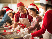 An Asian Family Spends Their Christmas Day Volunteering At A Charity Event. They Distribute Gifts, Food, And Warm Clothing To Underprivileged Families