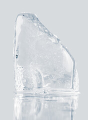 Wall Mural - Piece of crystal clear crushed ice block, isolated on a light gray reflective surface.