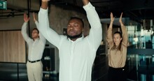 A Black business man in a white shirt is doing yoga with his colleagues in the office. Take a break from work to maintain spiritual strength and stability