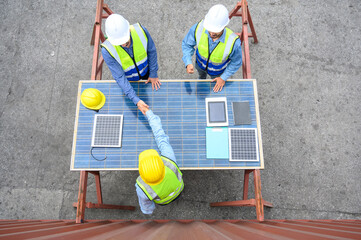 Top view of professional engineering people wearing helmets and safety vests meeting with solar photovoltaic panels handshake for agreement project. green alternative energy concept.