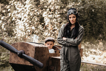 Wall Mural - A young aviator boy sits in a homemade airplane in a natural landscape. Next to her is an aviator mom in a helmet and glasses. The authentic mood of the picture. . Cartography. Vintage.