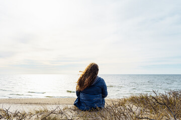 Long-haired curly plus size woman on the seashore, rear view