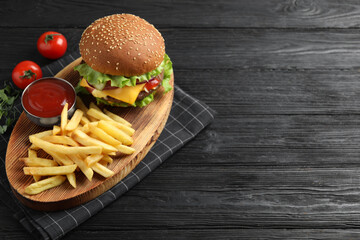 Delicious burger with beef patty, tomato sauce and french fries on black wooden table, above view. Space for text