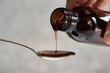 Herbal syrup being poured from a dark bottle onto a metal spoon