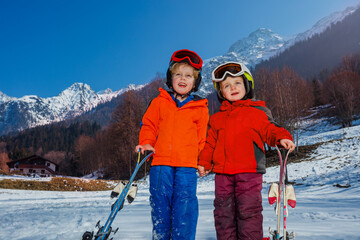 Portrait of two children enjoy first ski vacation, stand in snow