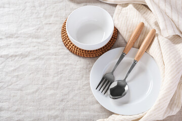 Wall Mural - White plate and bowl with spoon and fork  with linen napkin on tablecloth background