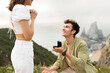 Happy young man standing on his knee and proposing to his girlfriend on a rocky cliff by the ocean shore