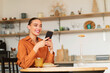 © Prostock-studio - Cheerful caucasian lady sitting at table in kitchen and using cellphone, shopping online from home, copy space