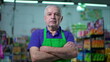 © Marco - One serious older employee of grocery store crossing arms with stern worried expression stands inside supermarket local shop