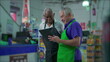 © Marco - Senior Supermarket Employees with Tablet Device, Teamwork Scene of Older Manager Instructing Colleague
