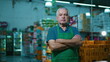 © Marco - Serious small business owner with arms crossed standing inside Grocery Store chain. Concerned preoccupied expression of an older supermarket manager wearing apron