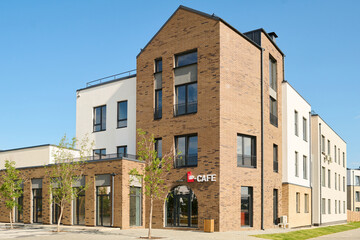 Wall Mural - Part of large street with corner of long three storey brick block of flats with cafe on facade standing by low building with glass doors