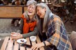 © Yaroslav Astakhov - Pretty senior Asian woman puts head on laughing friend shoulder resting together at table in street cafe on nice autumn day