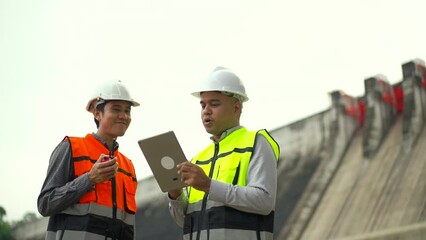 Wall Mural - Confident asian two engineers man inspection with in tablet at construction site dam with hydroelectric power plant and irrigation. Team engineer man working at project big building.