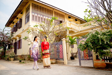 Wide shot of two young Asian women walk together in front of public ancient house in northern of Thailand that is landmark for the tourist.