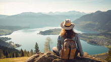 Woman With A Hat And Backpack Looking At The Mountains And Lake From The Top Of A Mountain In The Sunlight, With A View Of The Mountains