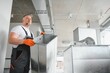 © Serhii - Man setting up ventilation system indoors. A male worker installs air ventilation pipes in a new office building.