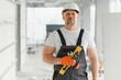 © Serhii - Portrait of a builder in working uniform with protective helmet standing with instruments at the construction site indoors