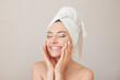 © Ольга Шефер - portrait of a young happy beautiful naked woman with closed eyes with a towel on her head smiling and gently touching her face with her hands. Isolated on a beige background