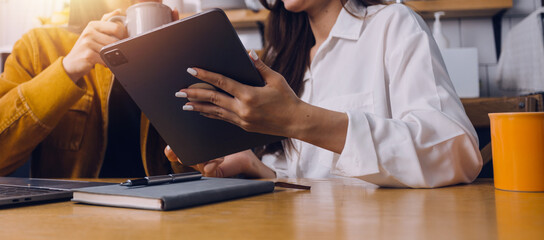 Female students note from the books at the Asian girl library sitting at sofa using laptop computer and tablet to search an online informations. in living room