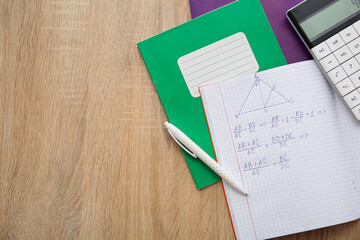 Open copybook with formulas, calculator and pen on wooden table