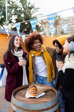 Diverse Group Of Young Friends Having Fun Drinking Hot Coffee And Eating Churros Or Fritters At Christmas Market On Winter Vacation. Millennial Student People Enjoying College Holidays.