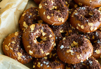 Sweet glazed chocolate donuts decorated with crumbs and almond flakes in box. Fresh pastries showcase