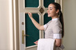 Young chambermaid with towels knocking on room door in hotel