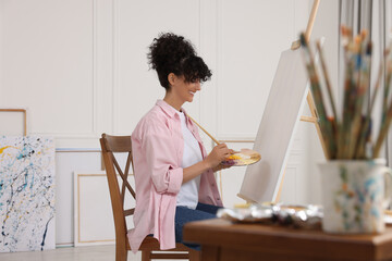 Poster - Young woman mixing paints on palette with brush near easel in studio