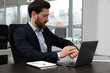 © New Africa - Man checking time on his watch while working with laptop at black desk in office