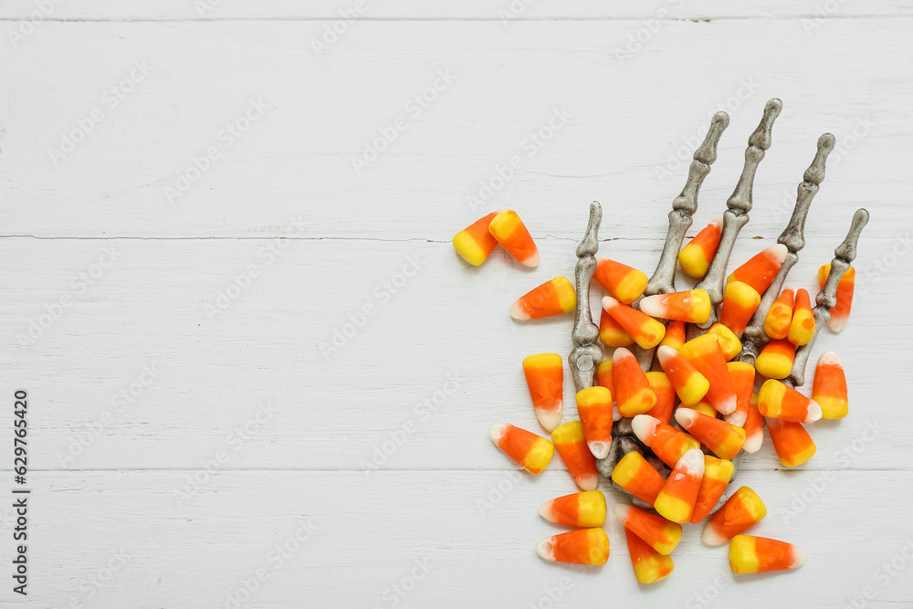 Tasty Halloween candy corns and skeleton hand on light wooden background