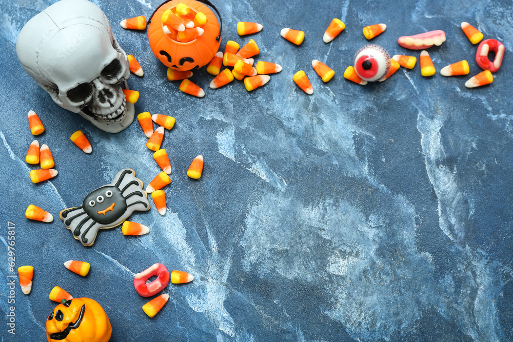 Composition with tasty Halloween candy corns, skull and cookie on blue background